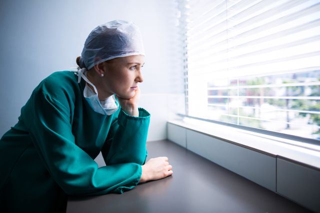 Thoughtful female surgeon looking through window - Download Free Stock Photos Pikwizard.com