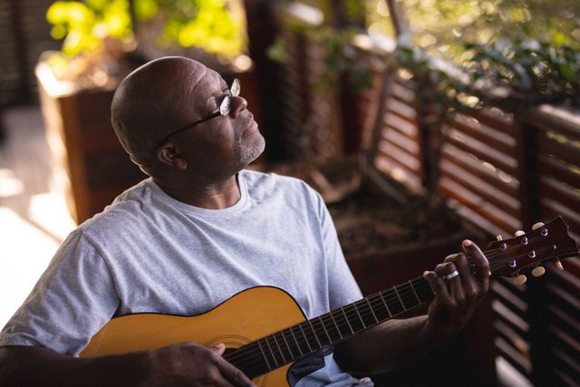 Relaxed african american senior man sitting in patio and playing guitar - Download Free Stock Photos Pikwizard.com