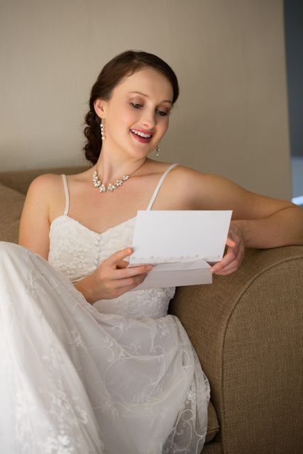 Happy bride reading wedding card while sitting on sofa - Download Free Stock Photos Pikwizard.com
