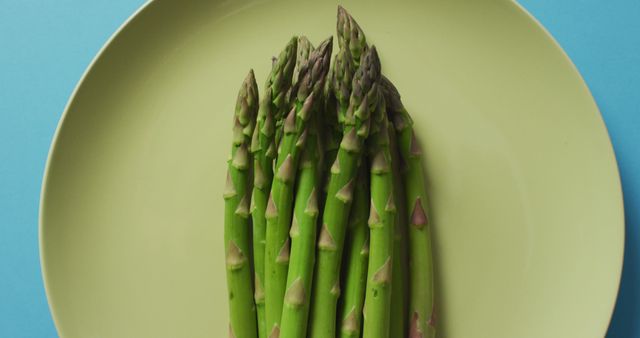 Image of fresh asparagus on green plate over blue background - Download Free Stock Photos Pikwizard.com