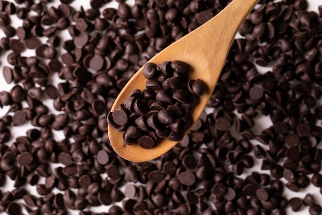 Close-up of chocolate chips in wooden spoon over white background, copy space. unaltered, sweet food, studio shot and indulgence.