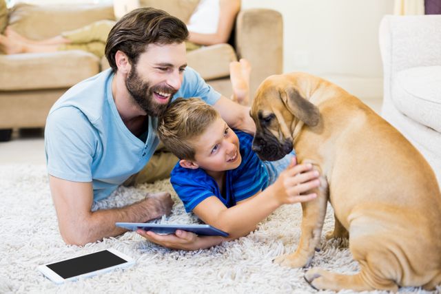 Father and son playing with a dog while using digital tablet at home