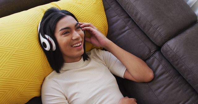 Gender fluid male wearing headphones enjoying listening to music while lying on the couch at home - Download Free Stock Photos Pikwizard.com