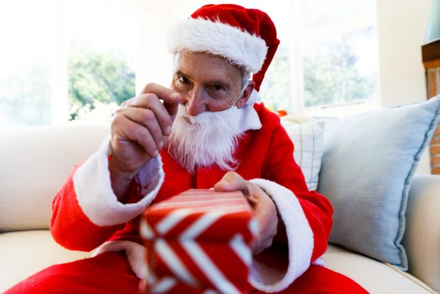 Front view of an old caucasian man wearing a santa clause costume holding out a christmas gift in fr - Download Free Stock Photos Pikwizard.com