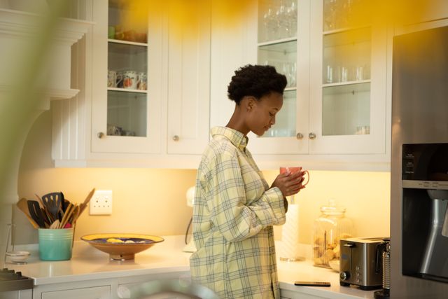 African American woman holding a coffee cup in the kitchen at home. Domestic life and spending time at home. 
