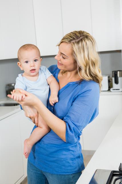 Mother holding her baby boy in kitchen - Download Free Stock Photos Pikwizard.com