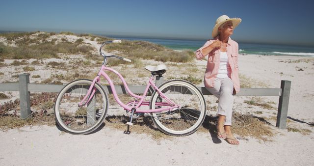 Happy senior caucasian woman sitting on fence with bicycle by the seaside - Download Free Stock Photos Pikwizard.com