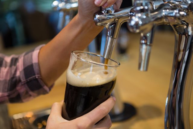 Cropped hands of barmaid pouring drink from tap in glass at bar counter
