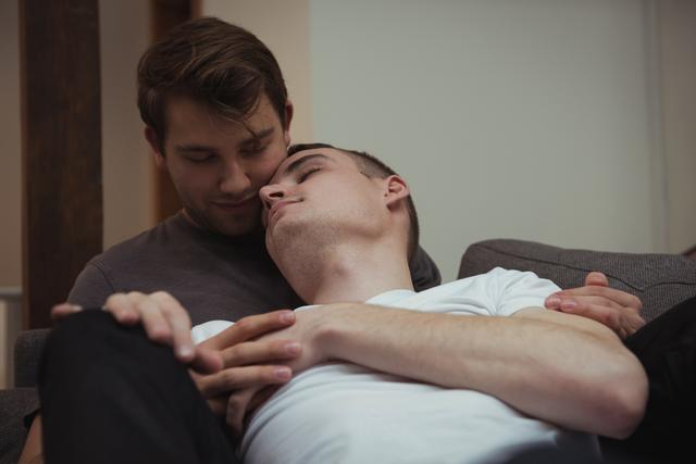 Romantic gay couple embracing on sofa in living room - Download Free Stock Photos Pikwizard.com