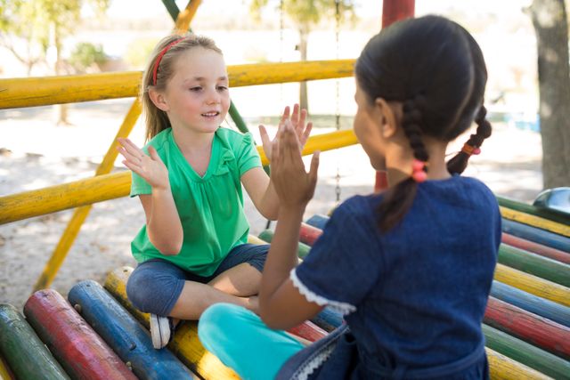 Girls playing clapping game while sitting on jungle gym - Download Free Stock Photos Pikwizard.com