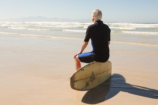 Rear view of senior man sitting on surfboard - Download Free Stock Photos Pikwizard.com