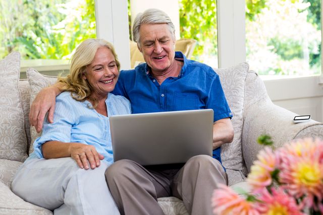 Senior couple using laptop while sitting on sofa - Download Free Stock Photos Pikwizard.com