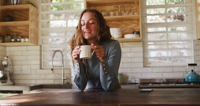 Happy caucasian woman enjoying drinking coffee, leaning on counter in sunny cottage kitchen. simple living in an off the grid rural home.