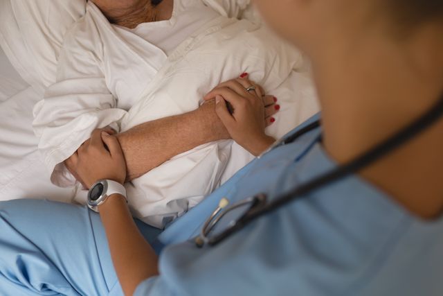 Mid section of female doctor consoling senior woman and holding her arm in bedroom at home