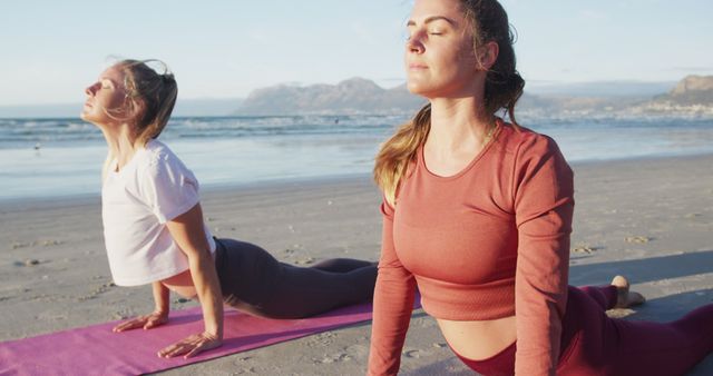 Two caucasian female friends practicing yoga, stretching at the beach. healthy active lifestyle, outdoor fitness and wellbeing.