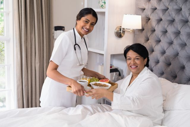 Smiling nurse serving breakfast to patient resting on bed at home - Download Free Stock Photos Pikwizard.com