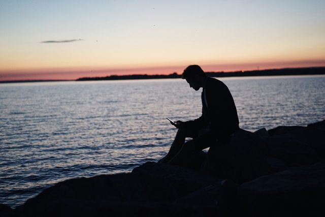 Silhouette of Sitting Man Near Calm Sea during Dawning Sunset - Download Free Stock Photos Pikwizard.com