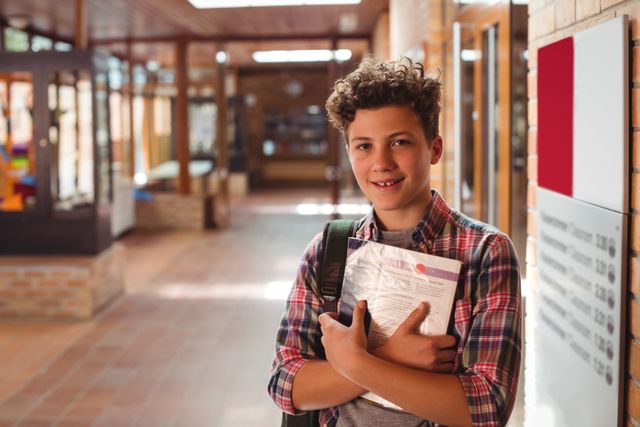 Portrait of schoolboy holding notebook in corridor - Download Free Stock Photos Pikwizard.com
