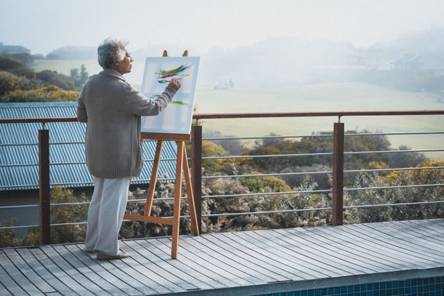 African american senior woman painting on canvas standing in the balcony at home - Download Free Stock Photos Pikwizard.com