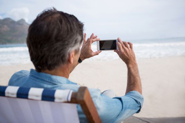 Rear view of man taking picture on mobile phone at beach - Download Free Stock Photos Pikwizard.com