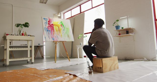 Rear view of thoughtful african american male artist sitting looking at his painting at art studio - Download Free Stock Photos Pikwizard.com