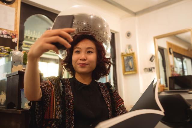 Stylish woman taking a selfie while sitting under a hairdryer- Download Free Stock Photos Pikwizard.com