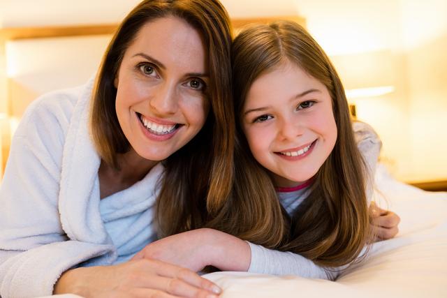 Portrait of happy mother and daughter lying on bed in bedroom