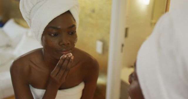 Smiling african american woman with towel watching in mirror and using pad on her face in bathroom - Download Free Stock Photos Pikwizard.com