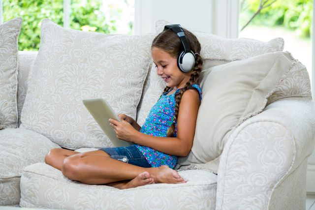 Cheerful girl using digital tablet while listening music on sofa at home