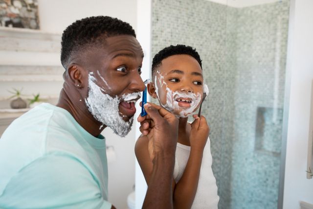 African american father and son shaving beards in bathroom. family life, spending time together at home.