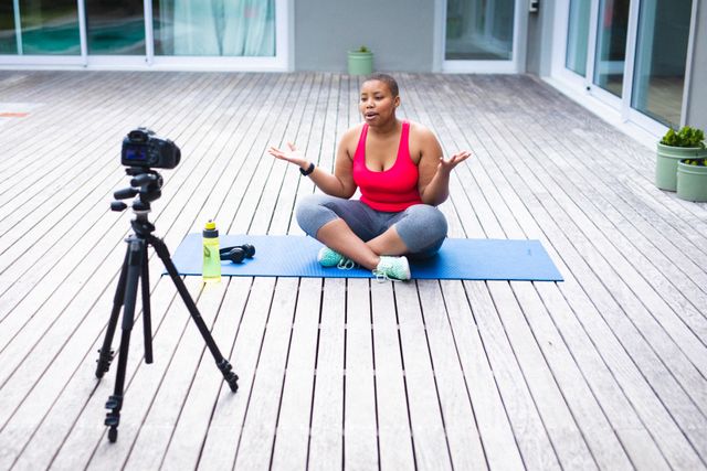 African american female blogger recording a video on digital camera while sitting on yoga mat - Download Free Stock Photos Pikwizard.com