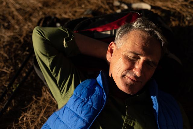 High angle front view of a senior Caucasian man enjoying time in nature, hiking in mountains on a sunny day, taking a break lying down smiling.