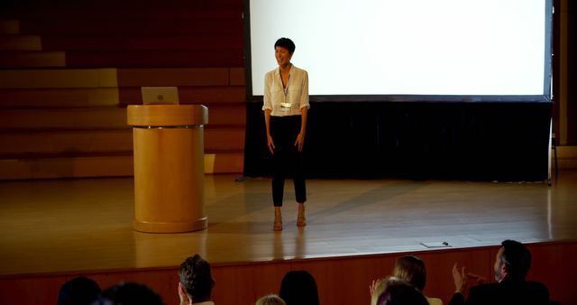 Front view of beautiful young Asian businesswoman speaking in business seminar in auditorium. Audience standing and applauding 4k