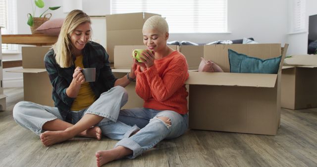 Happy diverse female couple with mugs of coffee sitting and moving home - Download Free Stock Photos Pikwizard.com