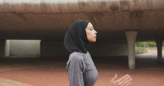 Side view of a mixed race woman wearing sportswear and hijab, exercising outdoors in the city on a sunny day, running in slow motion