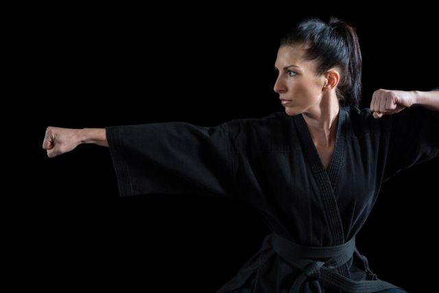 Female karate player performing karate stance against black background