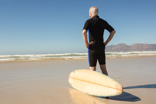 Rear view of man standing by surfboard against clear sky - Download Free Stock Photos Pikwizard.com