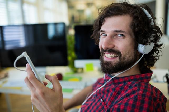 Male graphic designer listening music from mobile phone in office