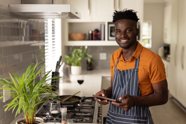 Portrait of smiling african american young man using digital tablet while cooking in kitchen at home - Download Free Stock Photos Pikwizard.com