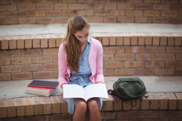 Attentive schoolgirl reading book in campus - Download Free Stock Photos Pikwizard.com