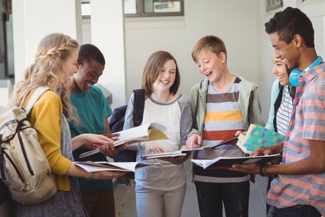Group of smiling students standing with notebook in corridor at school