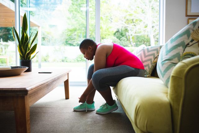African american woman tying her shoelaces while sitting on the couch at home - Download Free Stock Photos Pikwizard.com