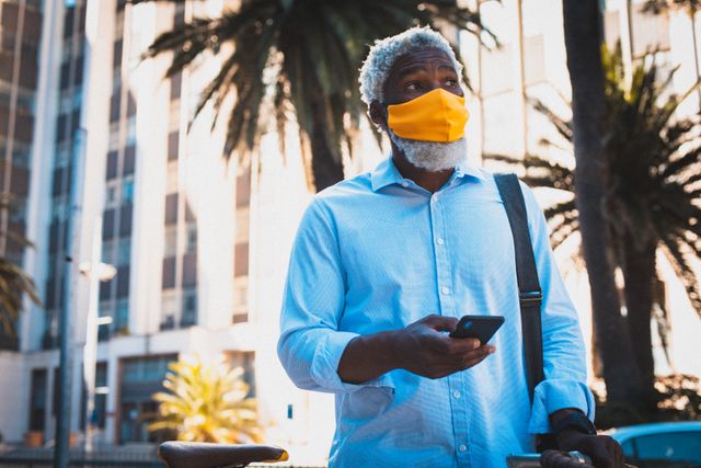 African american senior man wearing face mask using smartphone in the street - Download Free Stock Photos Pikwizard.com