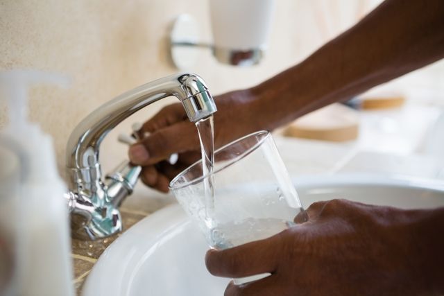 Cropped hands of man filling water in glass at bathroom sink