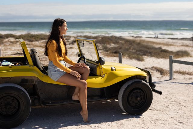 Smiling caucasian woman sitting on beach buggy admiring the view on sunny beach by the sea. beach stop off on summer holiday road trip.