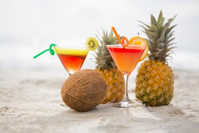 Coconut, pineapples and two glasses of cocktail drink kept on the sand - Download Free Stock Photos Pikwizard.com