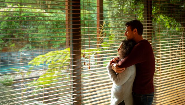 Diverse couple standing at window and embracing at home - Download Free Stock Photos Pikwizard.com