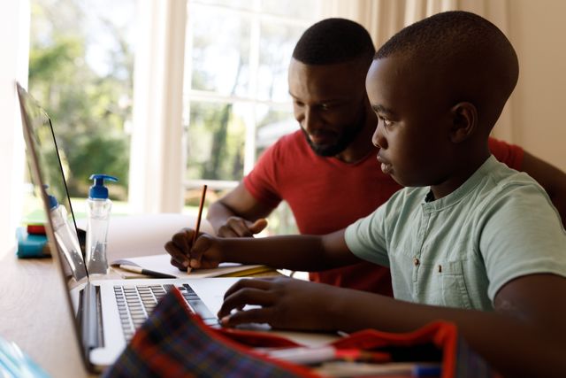 Side view of an african-american boy studying on a laptop with his father beside him helping - Download Free Stock Photos Pikwizard.com