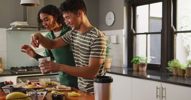 Happy diverse male couple making healthy drink together in kitchen. Spending quality time at home.