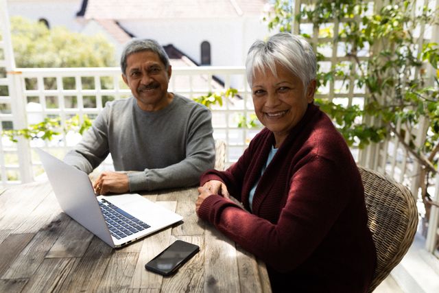 Senior african american couple sitting on terrace using laptop looking at camera and smiling - Download Free Stock Photos Pikwizard.com